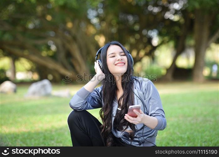 Asia woman listen to music with mobile phone outdoor / Happy young girl smiling relax exercise and listening to music with earphone on smartphones in the green garden park
