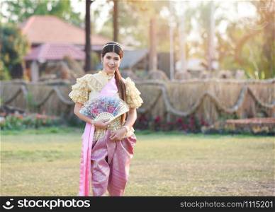 Asia woman thai style dress / Portrait of beautiful young girl smiling Thailand traditional costume wearing with paper fan in hand