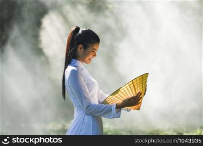 Asia woman vietnam or chinese style dress / Portrait of beautiful young girl vietnamese traditional costume wearing with hat weaving leaf in hand on nature background