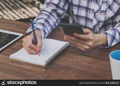 asia woman writing and holding phone on wood table in coffee shop