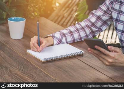 asia woman writing and holding phone on wood table in coffee shop