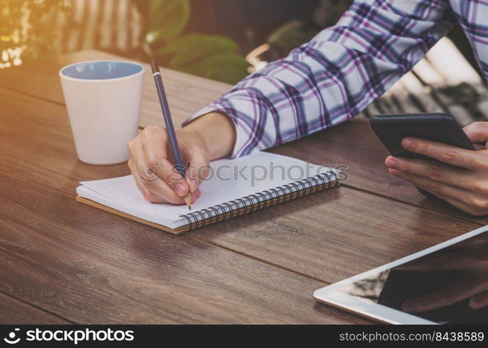 asia woman writing and holding phone on wood table in coffee shop. Vintage toned.