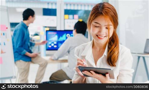 Asia young businesswoman using digital tablet talk to colleagues about plan in video call while smart working from modern office. Information technology, domestic lifestyle, or remote working concept.