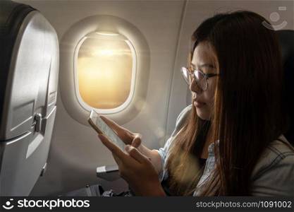 Asia young woman using the smart mobile phone while traveling inside the airplane beside the window, traveler and transportation concept