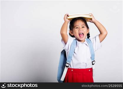 Asian adorable toddler smiling happy wear student thai uniform red skirt stand holding book over head and screaming in studio shot isolated on white background, Portrait little children girl preschool