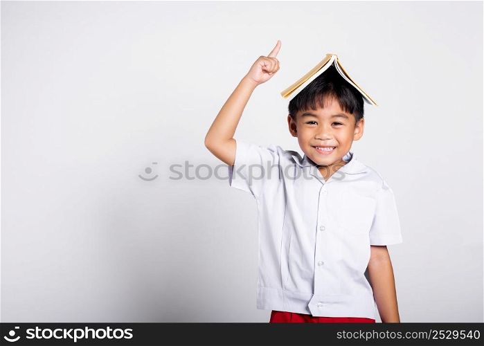 Asian adorable toddler smiling happy wearing student thai uniform red pants stand holding book over head like roof in studio shot isolated on white background, Portrait little children boy preschool