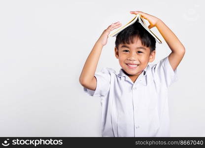 Asian adorable toddler smiling happy wearing student thai uniform red pants stand holding book over head like roof in studio shot isolated on white background, Portrait little children boy preschool