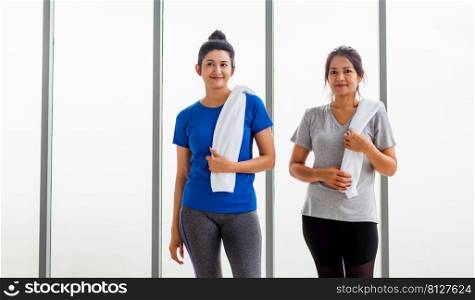 Asian adult and young woman smiling with towel around neck after yoga and exercise. Portrait of happy beautiful female standing indoor yoga studio, sport healthy workout concept