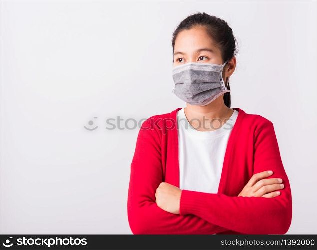 Asian adult woman stand crossed arm wearing red shirt and face mask protective against coronavirus or COVID-19 virus or filter dust pm2.5 and air pollution, studio shot isolated white background