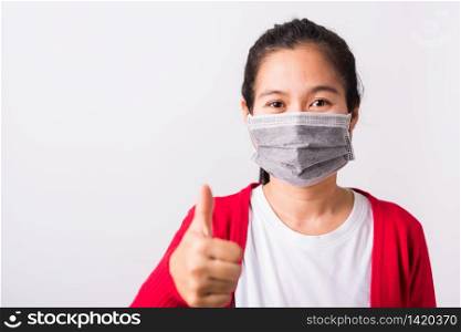 Asian adult woman wearing red shirt and face mask protective against coronavirus or COVID-19 virus or filter dust, air pollution her show finger thumb up for good sign, isolated white background