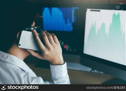 Asian agent trader man working and analysis in office and dealing with market financial charts and graphs and calling to customer.