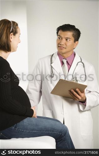 Asian American male doctor examining Caucasian pregnant female patient.