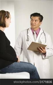 Asian American male doctor examining Caucasian pregnant female patient.