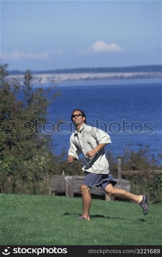Asian American Man Running After A Frisbee On A Campground Near A Lake