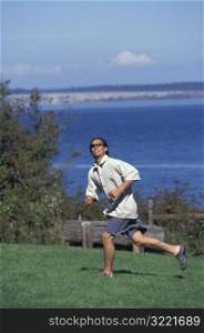 Asian American Man Running After A Frisbee On A Campground Near A Lake