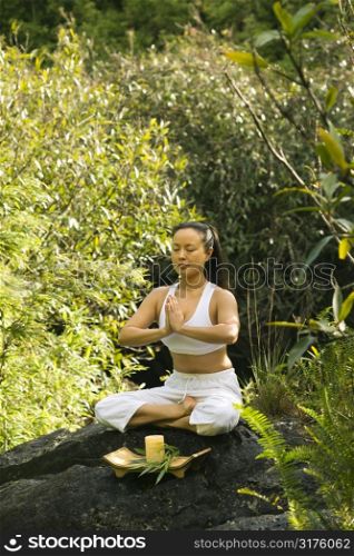 Asian American woman sitting on boulder in forest meditating with candle in Maui, Hawaii.