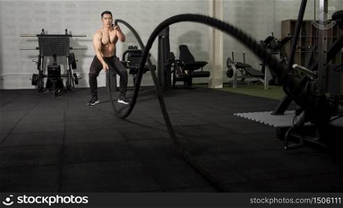 Asian athletic man with rope doing exercise in fitness gym