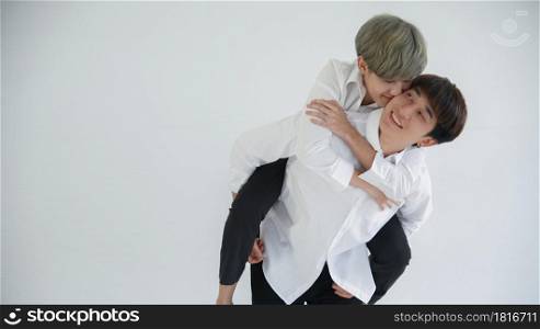 Asian attractive LGBT young gay couple hugging riding on back and kissing boyfriend's cheek in the room on white background