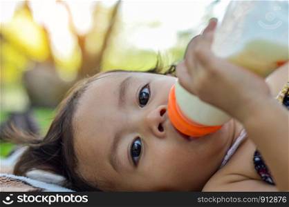 Asian baby girl eating milk from bottle in park