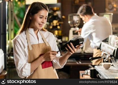 Asian Barista make payment with customer credit card using EMV chip technology for coffee purchase at a cafe bar.