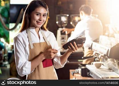 Asian Barista woman make payment with customer credit card using EMV chip technology for coffee purchase at a cafe bar. Cashless preventing from coronavirus covid-19 Spreading and infection.