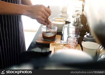 Asian barista young man making coffee according to order at counter bar with natural sunlight in the morning in modern cafe and restaurants.