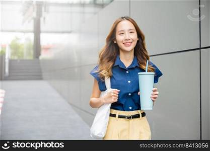 Asian beautiful business woman confident smiling with cloth bag holding steel thermos tumbler mug water glass she walking outdoors on street near modern building office, Happy female