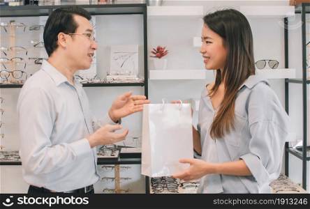 Asian beautiful female customer buying eyeglass from a man in departmentstore. Sales Discount and Promotion Concept.