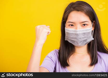 Asian beautiful happy teen young woman wearing face mask protective, COVID virus and air pollution her raise hands glad excited cheerful after recovering from illness isolated on yellow background