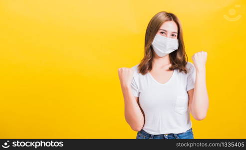 Asian beautiful happy young woman wearing face mask protection filter dust pm2.5, COVID virus and air pollution her raise hands glad excited cheerful after recovering from illness on yellow background