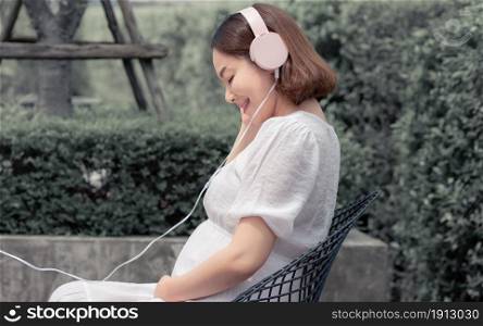 Asian beautiful pregnant mother listening to music with happy and sitting in the garden at home. Mother, Baby and Pregnancy Concept.