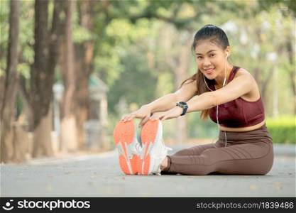 Asian beautiful sport woman with sportswear look at camera and smile during do body and legs stretching after exercise in park or garden.