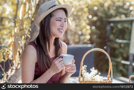 Asian beautiful woman wearing hat, smiling and drinking tea in the garden. Lifestyle, Summer and Travel Concept.