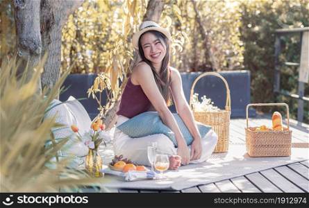 Asian beautiful woman wearing hat, smiling, going picnic and sitting in the garden. Lifestyle and Travel Concept.