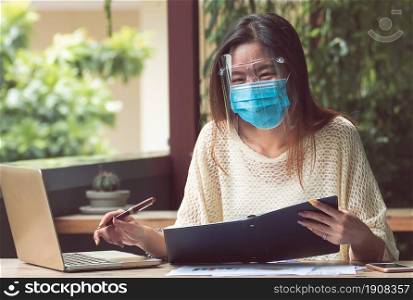 Asian beautiful woman wearing mask to protect virus and using laptop for working at home. New Normal and Technology concept.