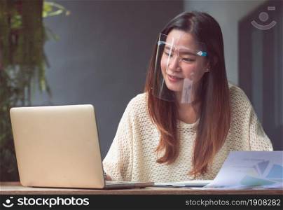 Asian beautiful woman wearing mask to protect virus and using mobile phone and laptop for working at home. New Normal and Technology concept.