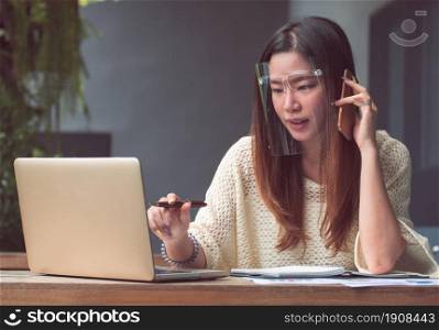 Asian beautiful woman wearing mask to protect virus and using mobile phone and laptop for working at home. New Normal and Technology concept.