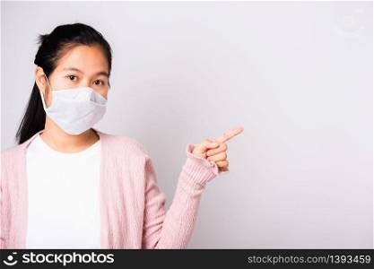 Asian beautiful woman wearing surgical protection face mask hygiene against coronavirus her pointing to side, studio shot isolated on white background with copy space, COVID-19 or corona virus concept