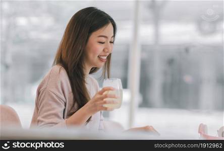 Asian beautiful young woman is smiling, drinking juice while resting at home. Lifestyle Concept.