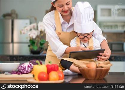 Asian beauty mother and cute little boy prepare online shopping and listing ingredient for cooking in kitchen at home with tablet. People lifestyles and Family. Homemade food and ingredient concept