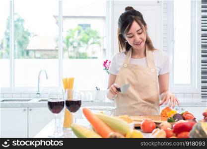 Asian beauty woman cooking and slicing vegetable in kitchen room with full of food and fruit on table. Holiday and Happiness concept. People and lifestyles concept. Family and dinner party theme.