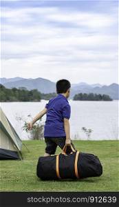 Asian boy holding bag Background grass and water at Kaeng Krachan Dam ,Phetchaburi in Thailand.