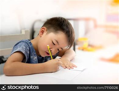 Asian boy is doing homework and writing with the intended face, Decorate the orange light, focus on the child.