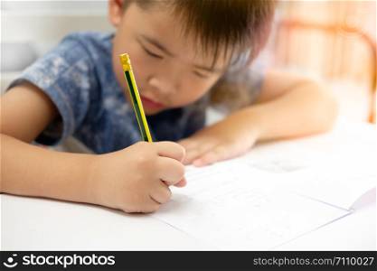 Asian boy is doing homework and writing with the intended face, Decorate the orange light, focus on the child.