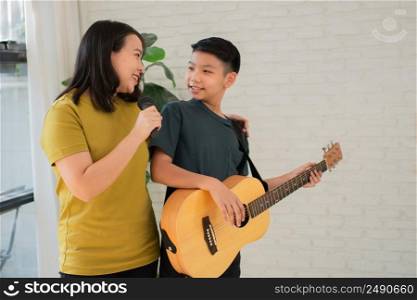 Asian boy playing guitar and mother sing a song and embrace, feel appreciated and encouraged. Concept of a happy family, learning and fun lifestyle, love family ties
