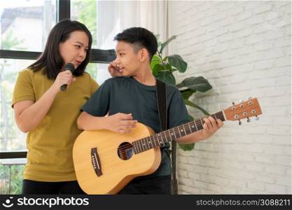 Asian boy playing guitar and mother sing a song and embrace, feel appreciated and encouraged. Concept of a happy family, learning and fun lifestyle, love family ties