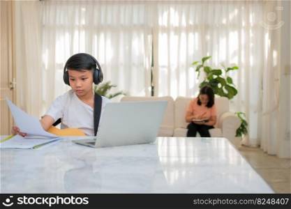 Asian boy playing guitar and watching online course on laptop while practicing for learning music or musical instrument online at home. Boy students study online with video call teachers play guitar.