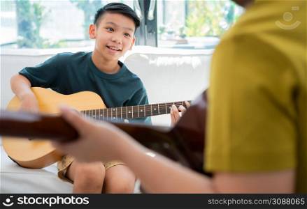 Asian boy playing guitar with father in the living room for teaching him son play guitar, feel appreciated and encouraged. Concept of a happy family, learning and fun lifestyle, love family ties