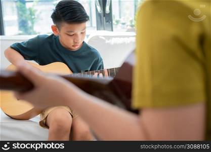 Asian boy playing guitar with father in the living room for teaching him son play guitar, feel appreciated and encouraged. Concept of a happy family, learning and fun lifestyle, love family ties