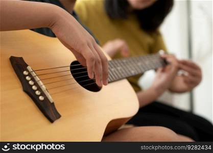 Asian boy playing guitar with mom in the living room for teaching him son play guitar, feel appreciated and encouraged. Concept of a happy family, learning and fun lifestyle, love family ties